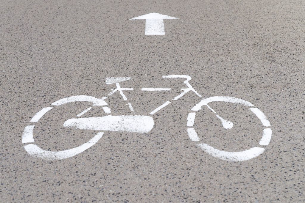 Road mark on asphalt indicating reserved bike path, grey background, bicycle silhouette and straight arrow