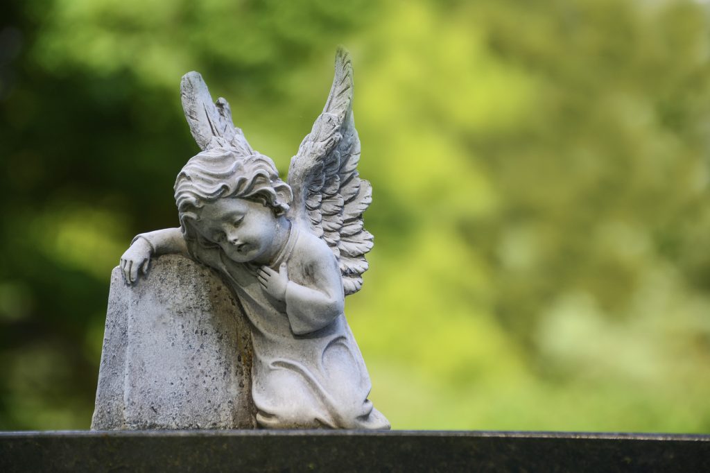Child angel statue on gravestone. Statue rests to empty small gravestone